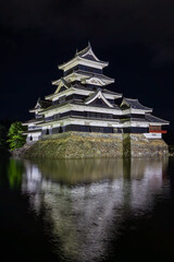 Old Japanese castle at night with reflection in its moat (Matsumoto Castle)