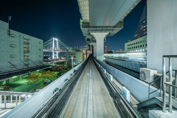 Yurikamome line at night with architectural landmark Rainbow Bridge in the distance in Tokyo, Japan.