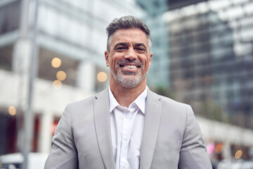 Smiling Latin 45 years old business man leader wearing suit standing on city street. Happy confident middle aged professional businessman entrepreneur wearing suit looking at camera outdoors. Portrait
