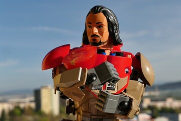 Fototapeta premium LEGO Star Wars Rogue One action figure of Baze Malbus, holding small half sliced red cherry tomato on his right arm, cityscape in background, blue skies with some clouds. 