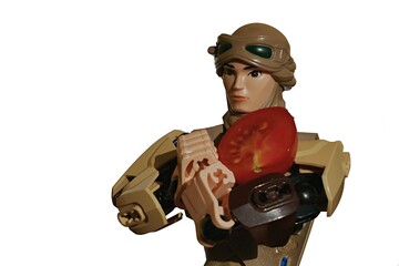 Naklejka premium LEGO Star Wars large action figure of Rey Skywalker in desert scavenger outfit, holding half sliced cherry tomato on her arms. 