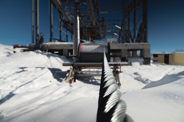 A cable car station under construction high in the mountains in winter. Focus on a close-up of a thick cable car cable covered with snow