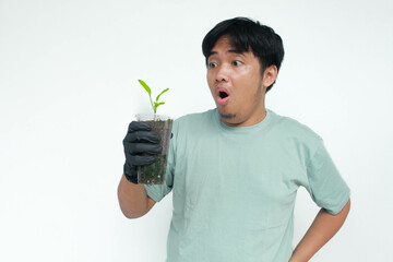 A young Asian man holds a vegetable plant pot made from used plastic bottles with an amazed...