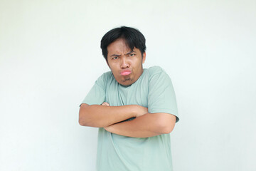 A young Asian man in a green t-shirt with an angry and annoyed expression. Isolated in gray...