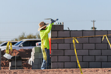 A mason worker reading a spirit level atop a block of a concrete fence he is building at a...