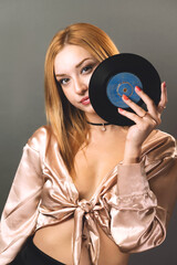 A young woman gazes through the center of a vinyl record, merging fashion with music nostalgia - 777427554
