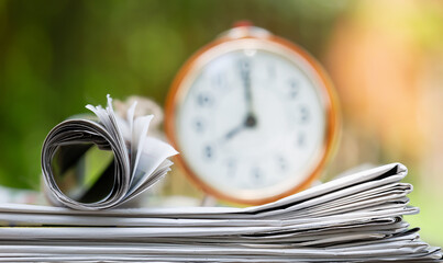 Stack of newspapers with alarm clock. Daily news, journalism background.