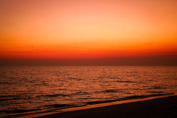 The sea after sunset has an orange glow and an orange sky with no clouds.