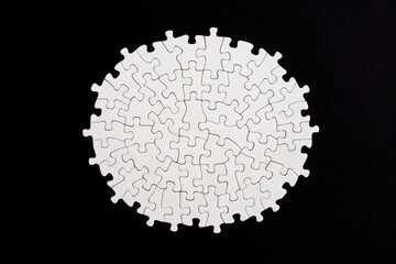 Plain white jigsaw puzzle  on black color background, oval shaped frame, abstract backdrop