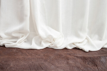 White fabric drapes folds on a brown leather stage or desk, abstract backdrop
