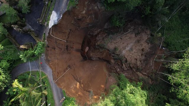 Top-down aerial shot of dangerous landslide destroyed village road. Camera look down and roll, showing unusual perspective of steep bluff and house buildings standing close to edge.