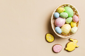 Colorful Easter eggs in wicker basket against colored background, closeup. top view with copy space