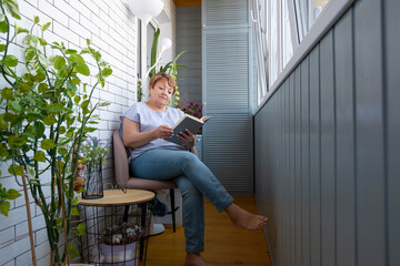 Senior woman relaxing on home balcony reading a book after work. Lifestyle outdoors