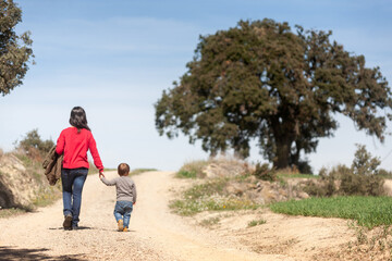 Mother and her young son walk along a path towards an oak tree.