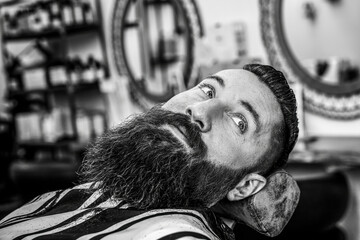 Black and white perspective of a modern man's grooming session. A barber's skillful touch transforms a beard in a vintage-inspired salon setting.