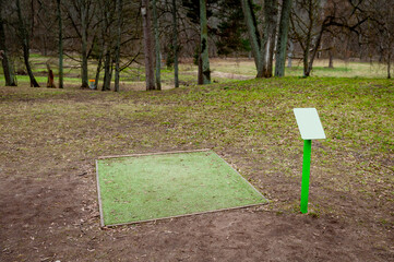 A green recreational area  for outdoor disc golf in erly spring. Drop zone with artificial grass and map. Outdoor recreational sports equipment, no people around. Vilce Manor, Latvia, Baltic.