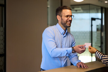 Smiling businessman working in an office building, taking a card for a door-opening.