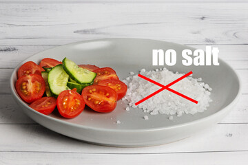 On a gray plate there is a mix of vegetables and a pile of sea salt, crossed out with a red cross. The inscription - no salt. Healthy eating concept