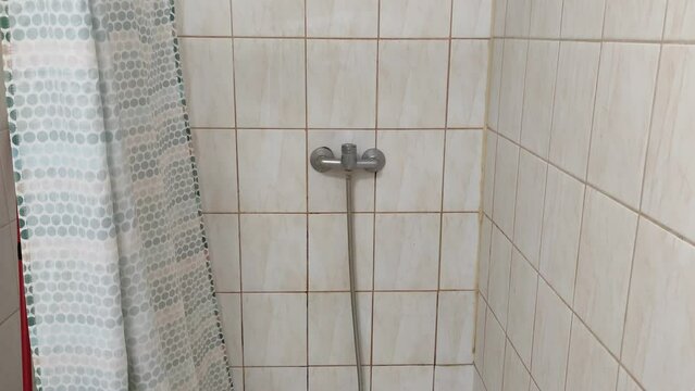 Old dirty tiled bathroom with shower and dirty floor in a cheap hostel or student dormitory