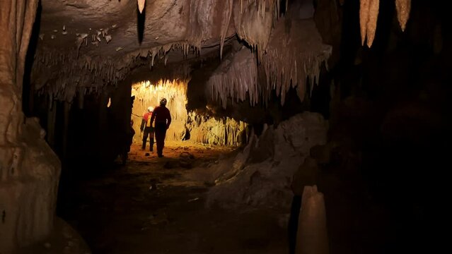 A group of speleologist inside a cave, illuminated by headlamps, exploring the depths of a mysterious underground system. High quality 4k footage