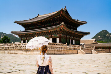 Naklejka premium Seoul, South Korea. Gyeongbokgung Palace. Woman in hanbok, traditional Korean dress, costume and clothes. Travel tour and tourism at landmark and tourist attraction. Back view of lady with umbrella.