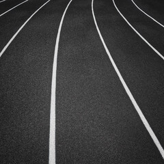 Track and Field Running Lanes. Overhead view of a rubber black running track surface with white lane lines. There is a slight curve of the white lane lines. Rubber black surface.