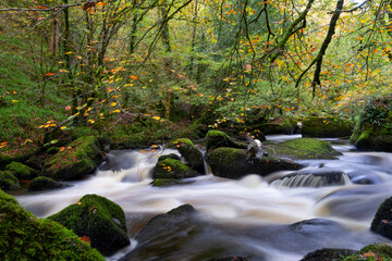Pose longue en automne : la rivière argentée traverse un paysage de rochers polis et de feuillage aux teintes chaudes.