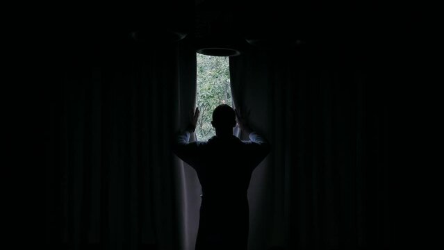 young man stands by the panoramic window and opens the curtain	