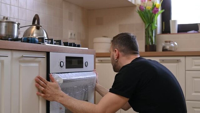 Close-up of oven installation in kitchen. Man installing household appliances at home