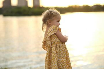 two-year-old faces a lake, her small hand gripping fresh-picked daisies. A poignant reminder of...