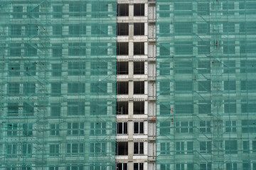 A high-rise building in the process of construction, covered with green safety netting © sommersby
