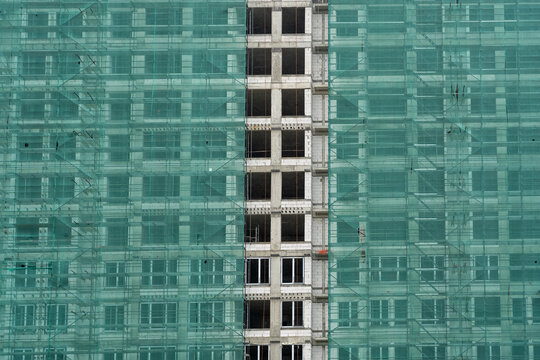 A high-rise building in the process of construction, covered with green safety netting