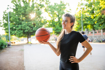 A woman is holding a basketball in a park ready to play a game