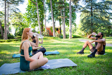 A group of sporty people are sitting on the grass in a park, drinking water