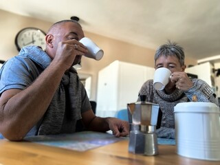Adult couple, sitting at the table, during breakfast, drinking coffee. Stormy awakening. Couple problems. Post discussion - obrazy, fototapety, plakaty