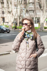 Beautiful stylish young woman with sunglasses eats ice cream walking on the street