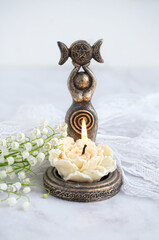 amulet of Triple Goddess figurine, floral candle and lilies of the valley flowers close up,...
