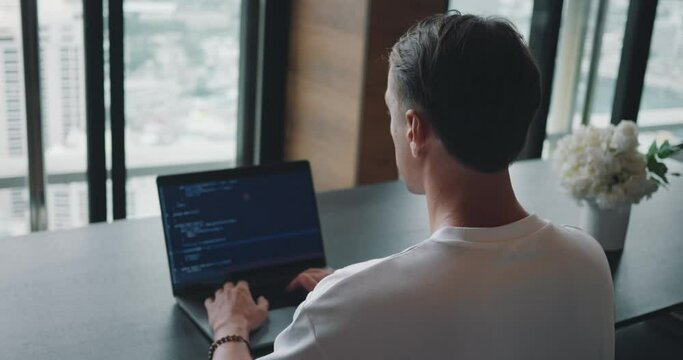 Software engineer at work as he skillfully crafts code on his laptop, providing an inside look at programming in action. Programming Professional, Man Crafting Code on Laptop Seen from the Back