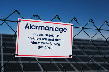 Hinweis auf Alarmanlage am Zaun einer Solaranlage