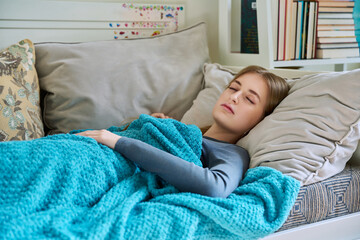 Sleeping young teenage female, under blanket at home on couch