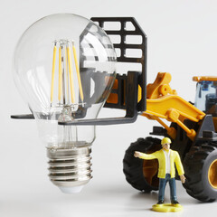 Toy tractor and a labourer prepare to install and mount an LED lamp. Transport, loading, unloading and installation services for fragile electrical goods. Photo