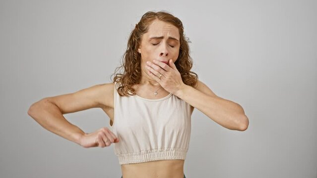 Young woman stifling a bored yawn, standing isolated on a white background, exuding sleepiness and fatigue