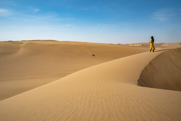 Fototapeta na wymiar Frau in gelbem Kleid steht auf einer Sanddüne, blickt in die Wüste Namib