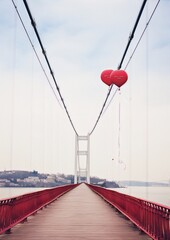 Red heart balloons float over a bridge, a pathway to a distant horizon.
