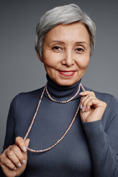 Elegant mature woman in smart casualwear looking at camera while standing in isolation on grey background during photo session