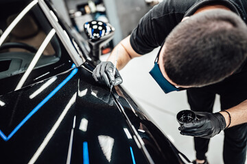 Professional worker fixing luxury car scratches at car detailing and valeting service center....