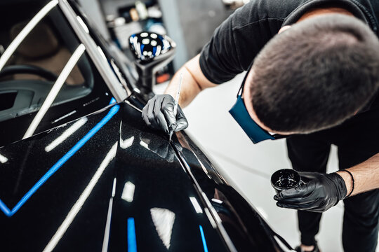 Professional worker fixing luxury car scratches at car detailing and valeting service center. Selective focus.