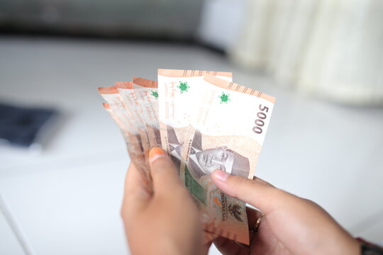 A woman's hand holds five thousand Indonesian notes for the Eid al-Fitr holiday