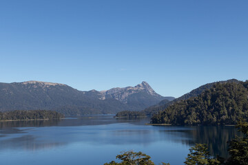 Majestic nature view of a huge clear blue lake reflecting the forest that surrounds it and the...