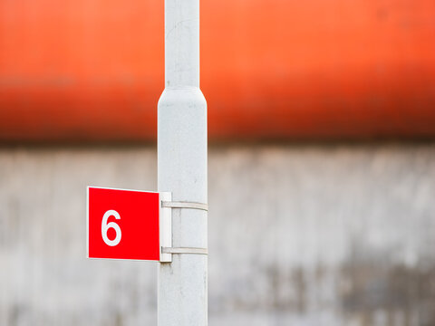 Red Number 6 Sign Attached to a Grey Pole in Front of a Bridge